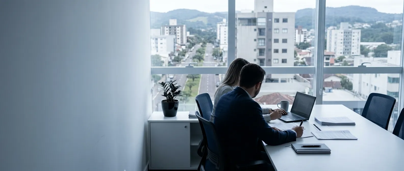 Consultor e cliente em reunião à mesa do escritório, com notebook e documentos